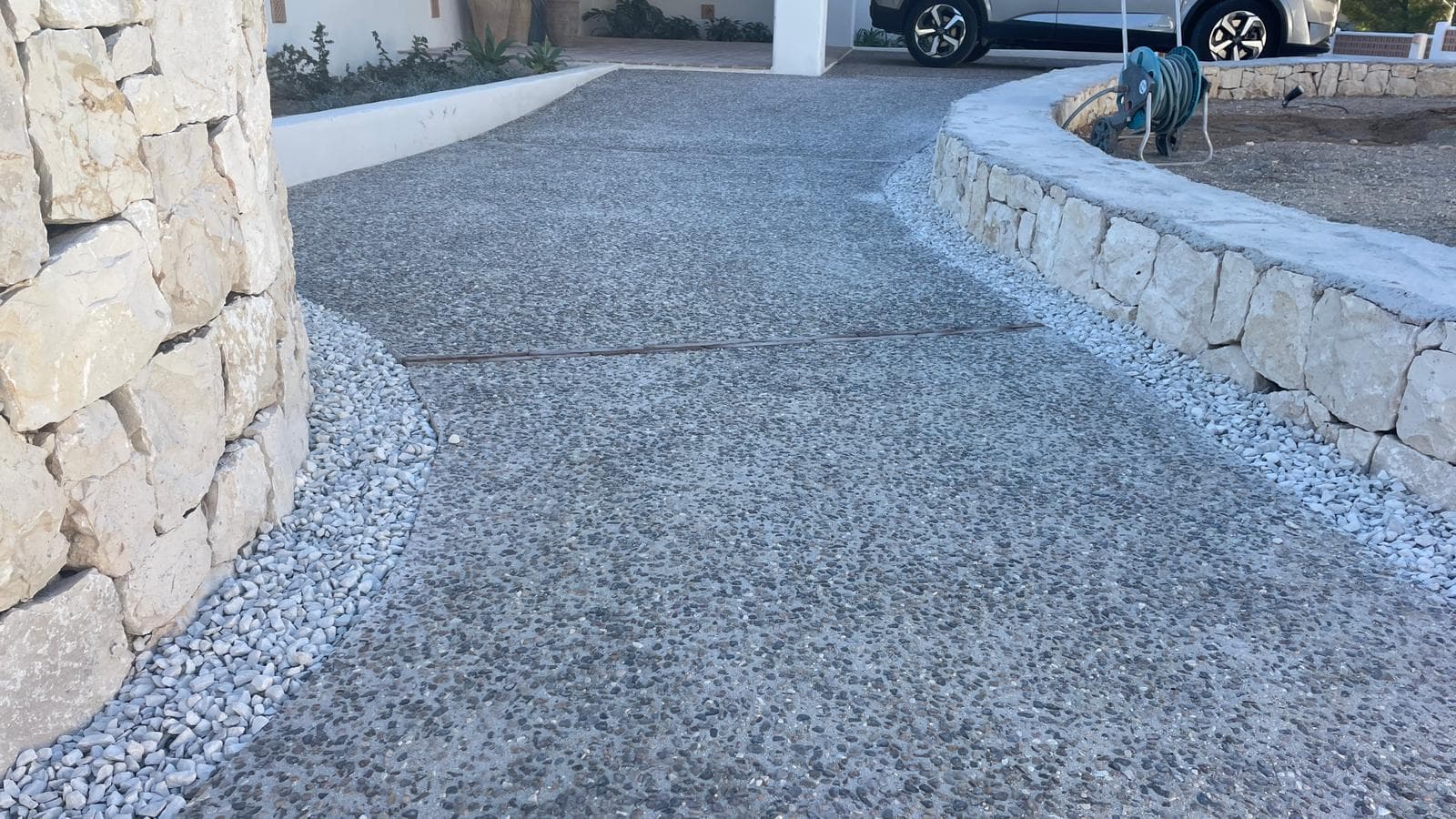 Rampa de hormigón desactivado con la piedra vista, entre muros de mampostería, ante la entrada de una vivienda.