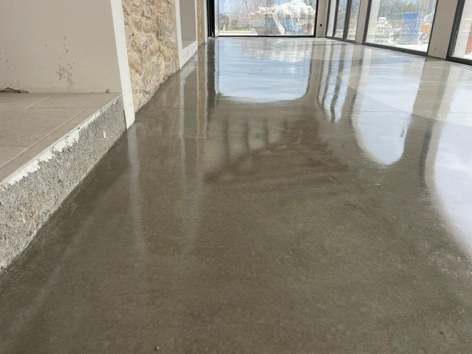 Interior diáfano con solera de hormigón pulido gris que refleja el ventanal como un espejo.