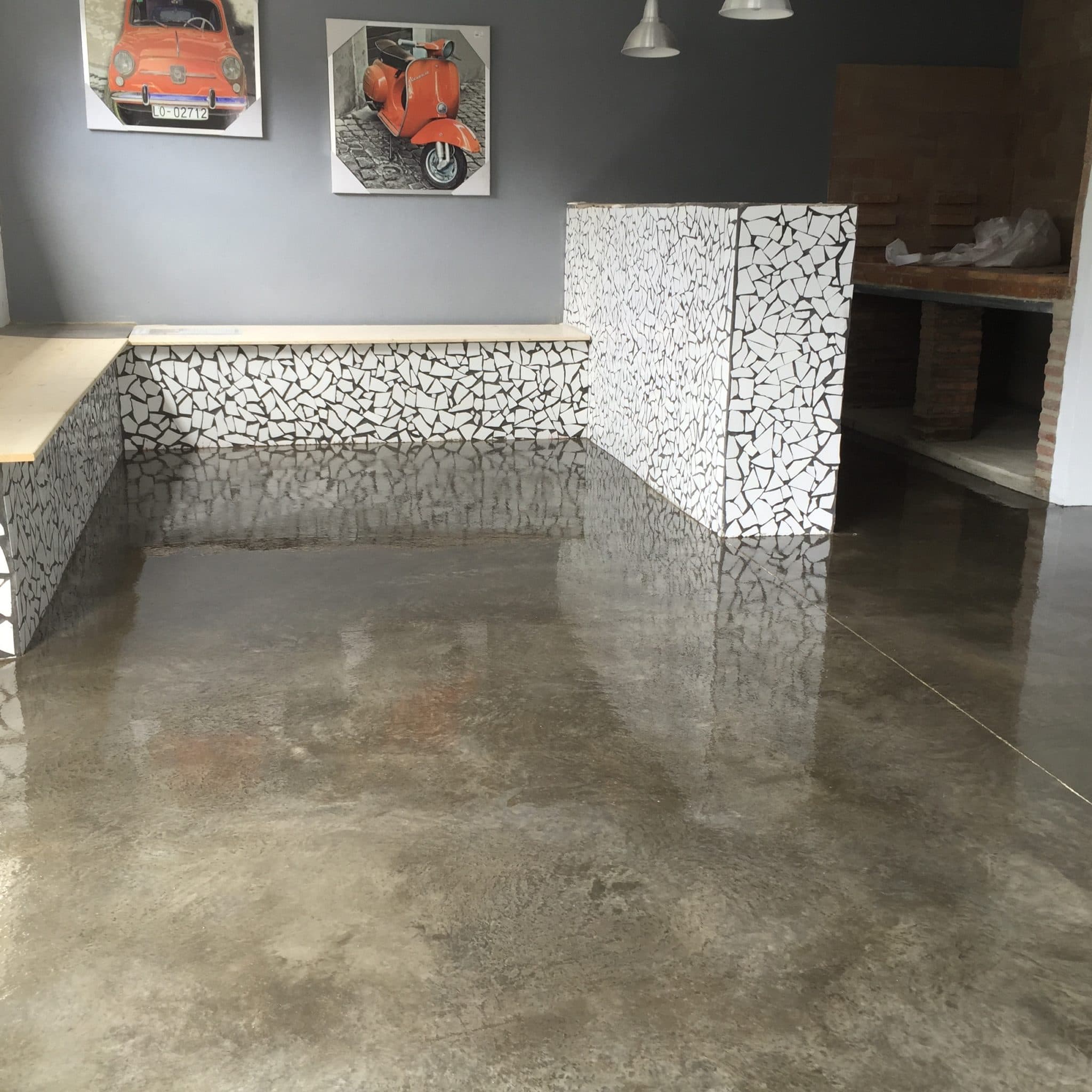 Estancia con suelo y banco corrido de microcemento gris, con láminas enmarcadas en la pared.